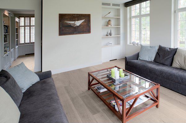 Salon lumineux avec canapés gris, table basse en bois et grandes fenêtres.