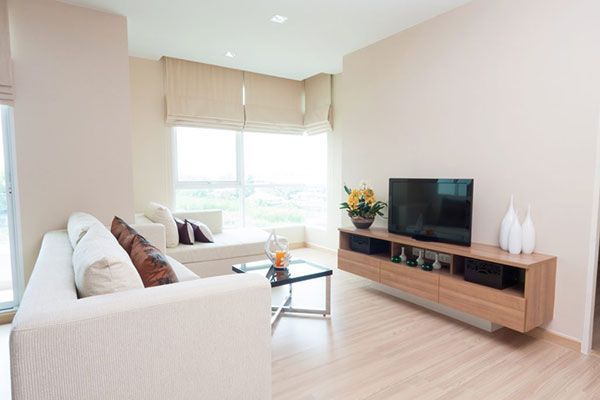 Salon minimaliste et lumineux avec canapé blanc, meuble TV en bois et grande fenêtre avec stores.
