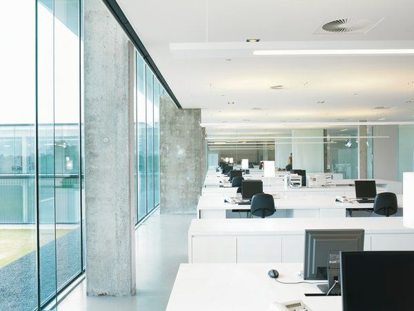 Bureau moderne et lumineux avec murs de verre, rangées de bureaux blancs et ordinateurs donnant sur une vue sur la ville