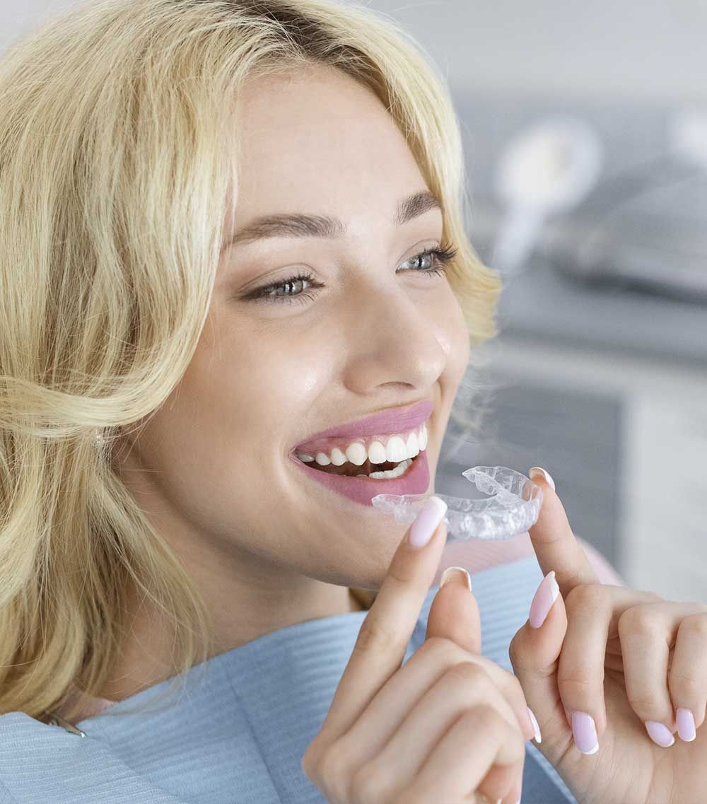 Una mujer sonríe mientras sostiene un aparato transparente en su boca.
