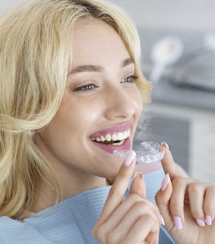 Una mujer sonríe mientras sostiene un aparato transparente en su boca.