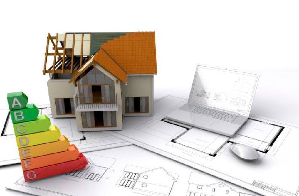 Casa modelo en construcción con tabla de calificación de eficiencia energética, planos arquitectónicos y computadora portátil.