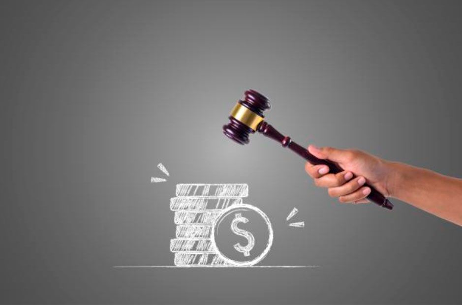 Mano sosteniendo un mazo sobre una pila de dinero con un símbolo de dólar.