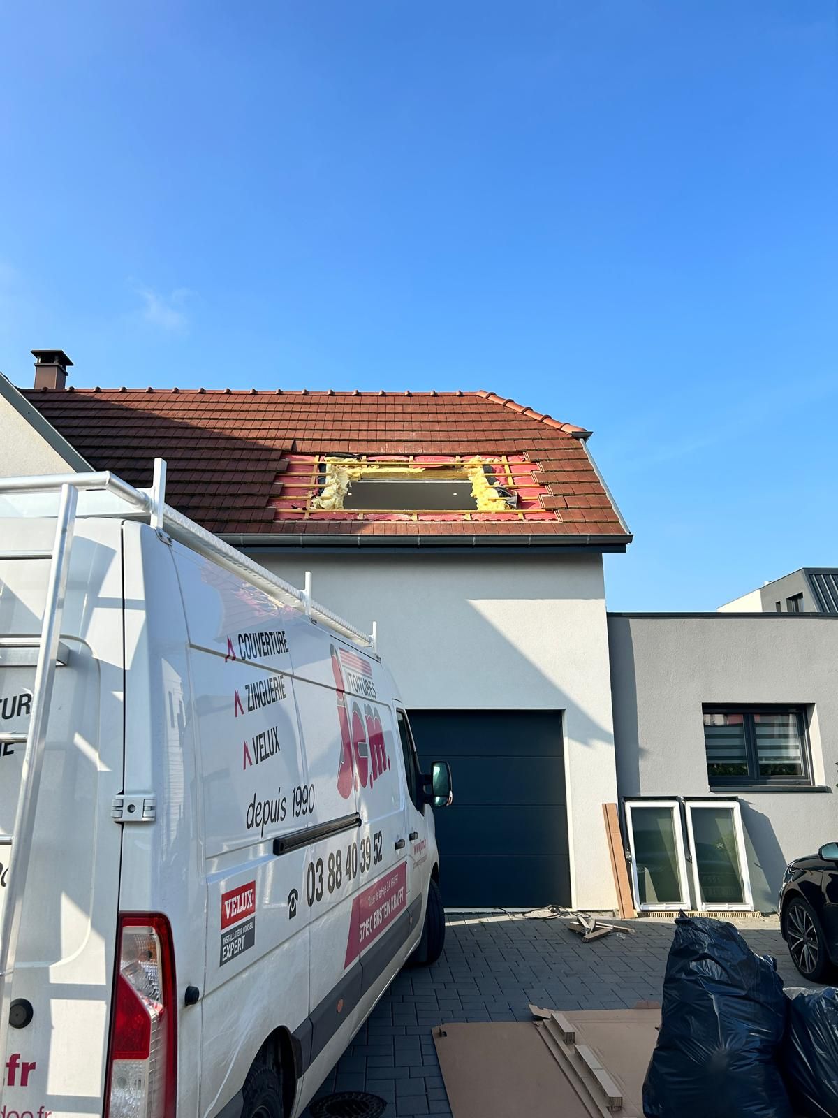 Une camionnette blanche est garée devant une maison en rénovation, le toit est partiellement ouvert.