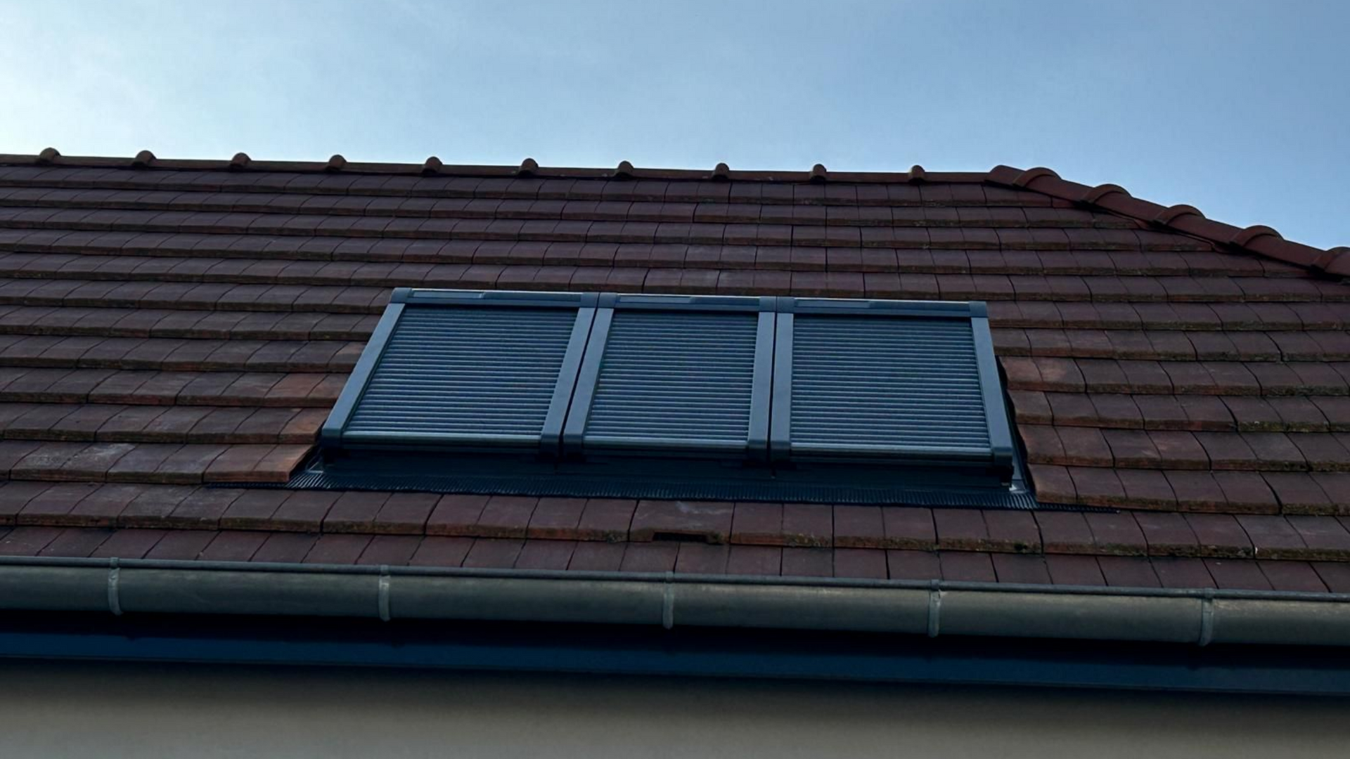 Puits de lumière sur un toit de tuiles rouges, se détachant sur un ciel bleu limpide.