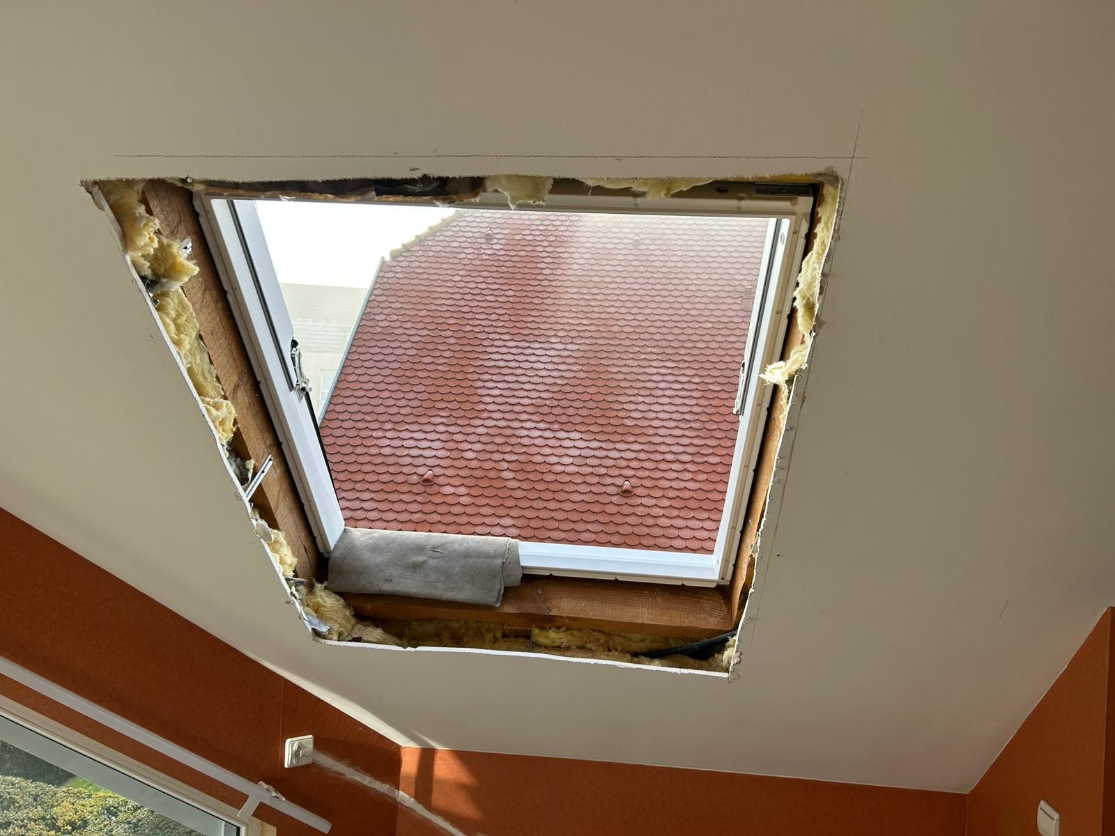 Fenêtre de toit installée au plafond, laissant apparaître l'isolation sur les bords. Vue sur le toit et le ciel.
