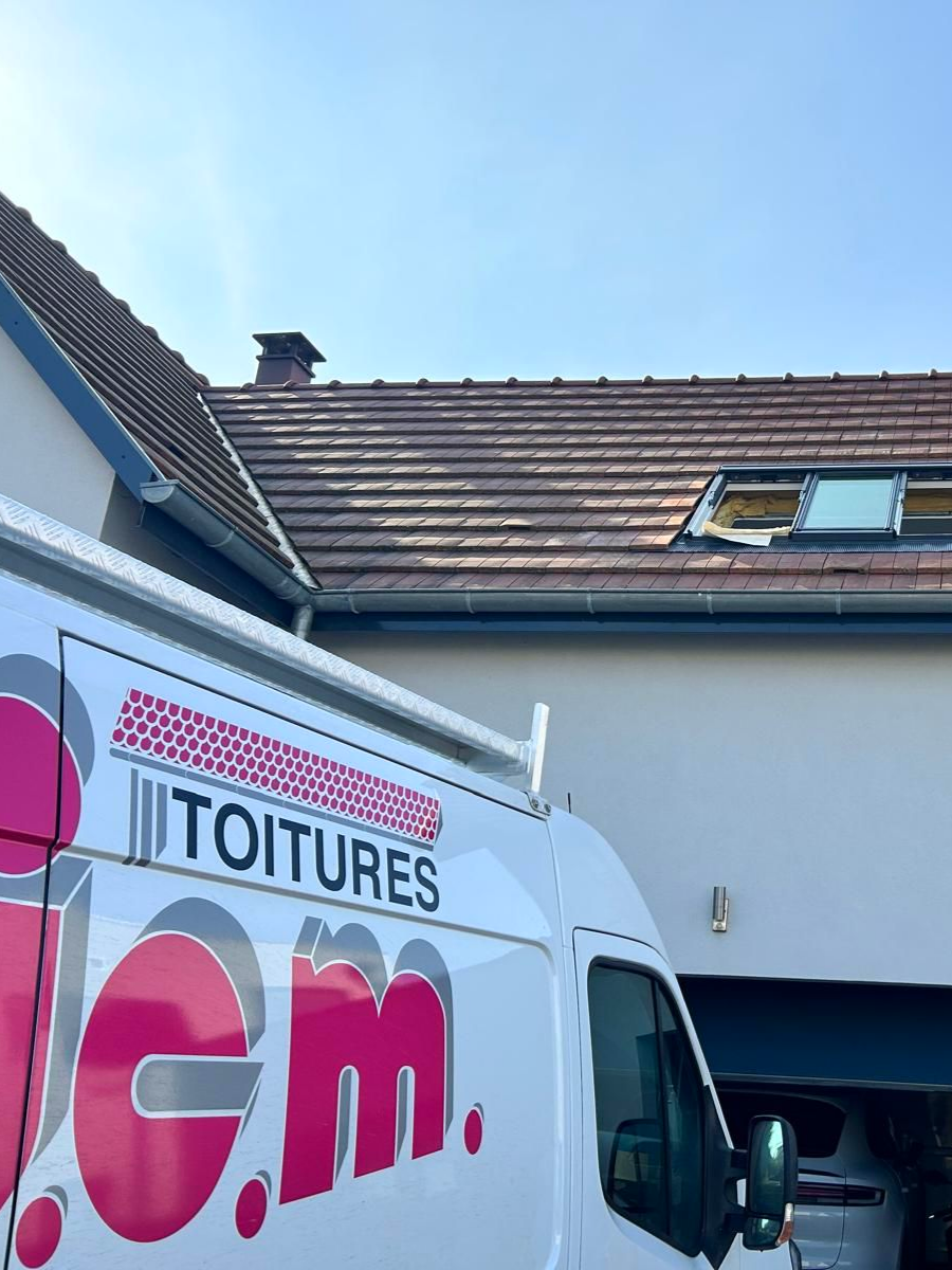 Une camionnette blanche est garée près d'une maison avec un toit en tuiles et un puits de lumière.