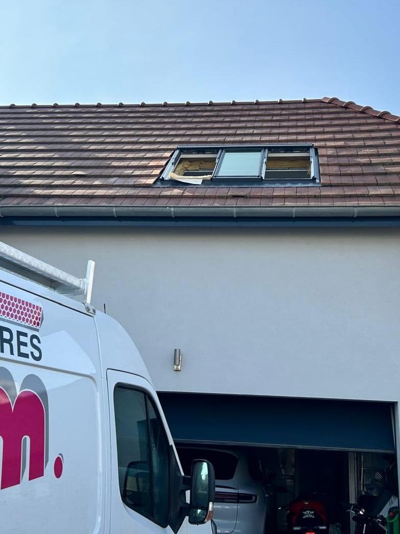 Une camionnette blanche avec un logo est garée près d'une maison avec un garage ouvert et une fenêtre de toit.