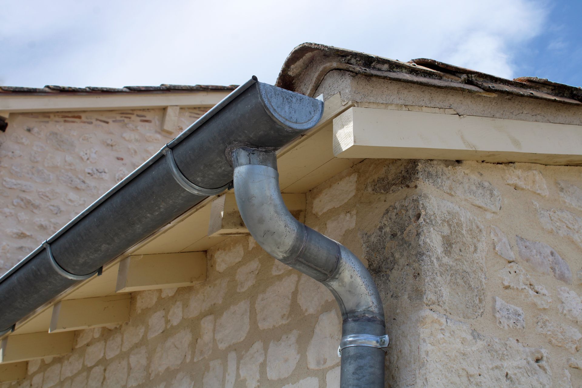 Système de gouttières grises sur un bâtiment en pierre.