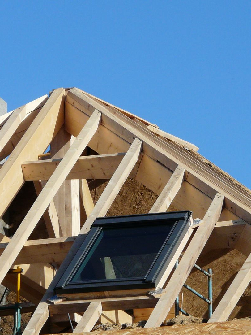 Charpente en bois avec puits de lumière sur fond de ciel bleu azur. Travaux en cours.