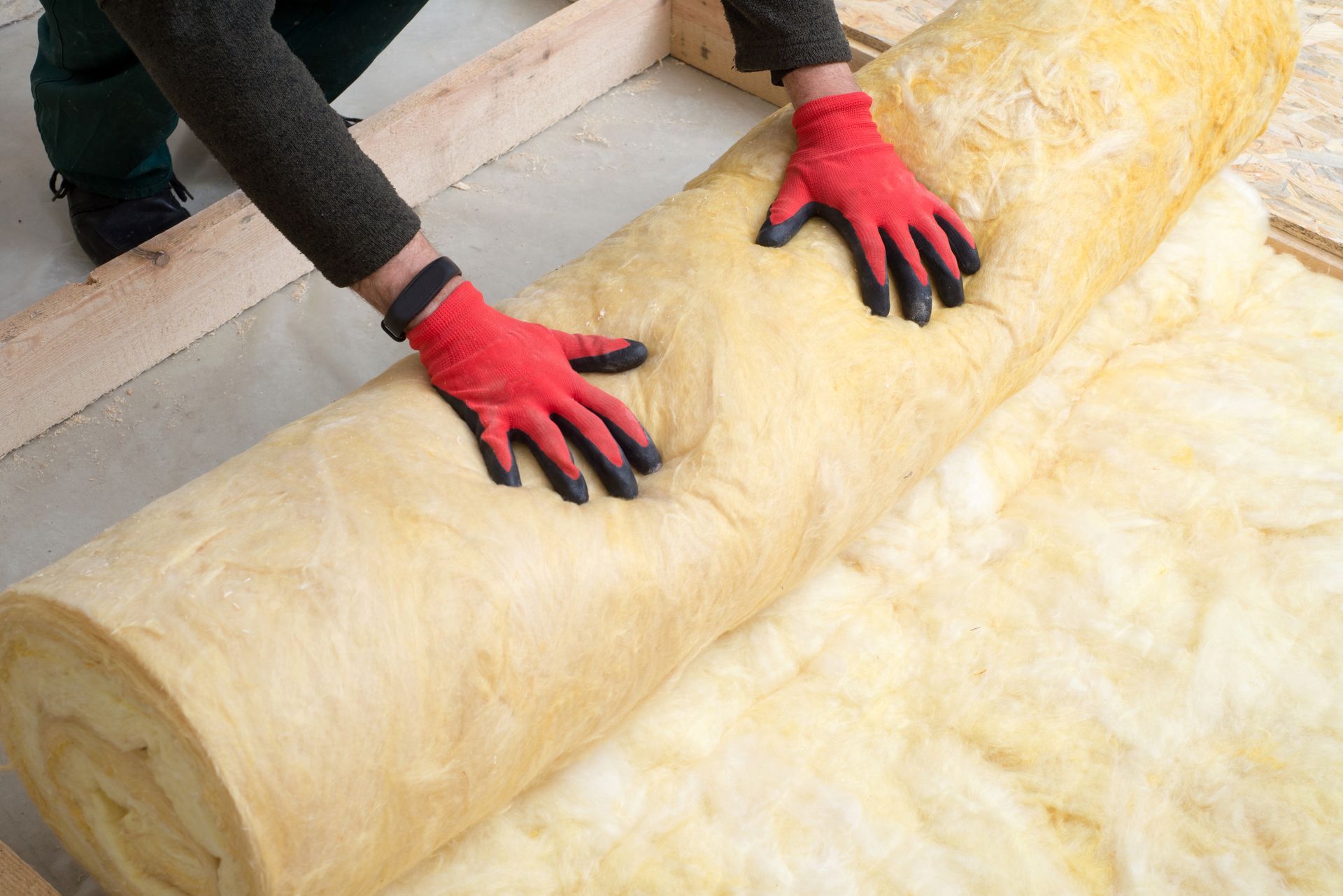 Une personne portant des gants rouges déroule l'isolant dans un cadre en bois.
