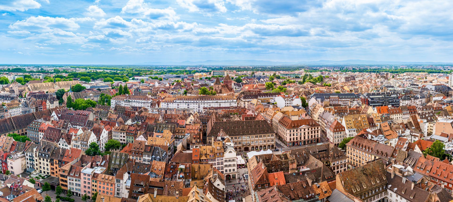 Vue aérienne de la ville de Strasbourg avec un ciel bleu parsemé de nuages cotonneux.