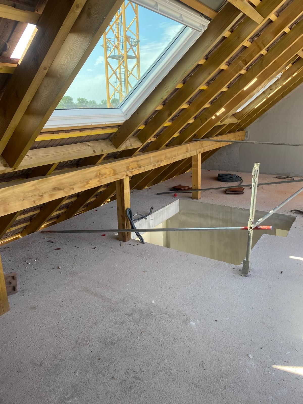 Combles en cours d'aménagement avec puits de lumière, poutres apparentes et ouverture dans le plancher.