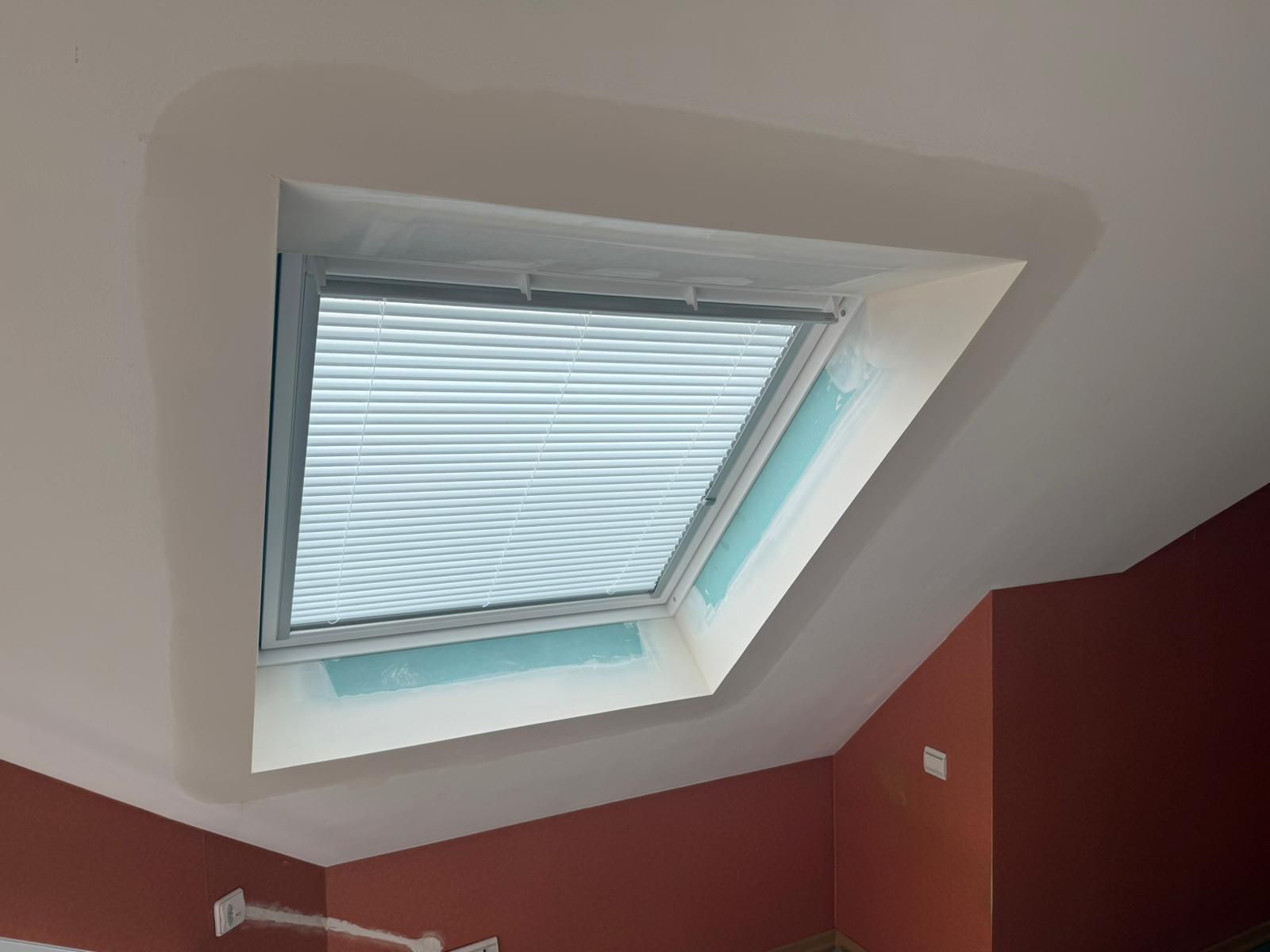 Fenêtre de toit avec stores fermés, plafond blanc et murs rouges.