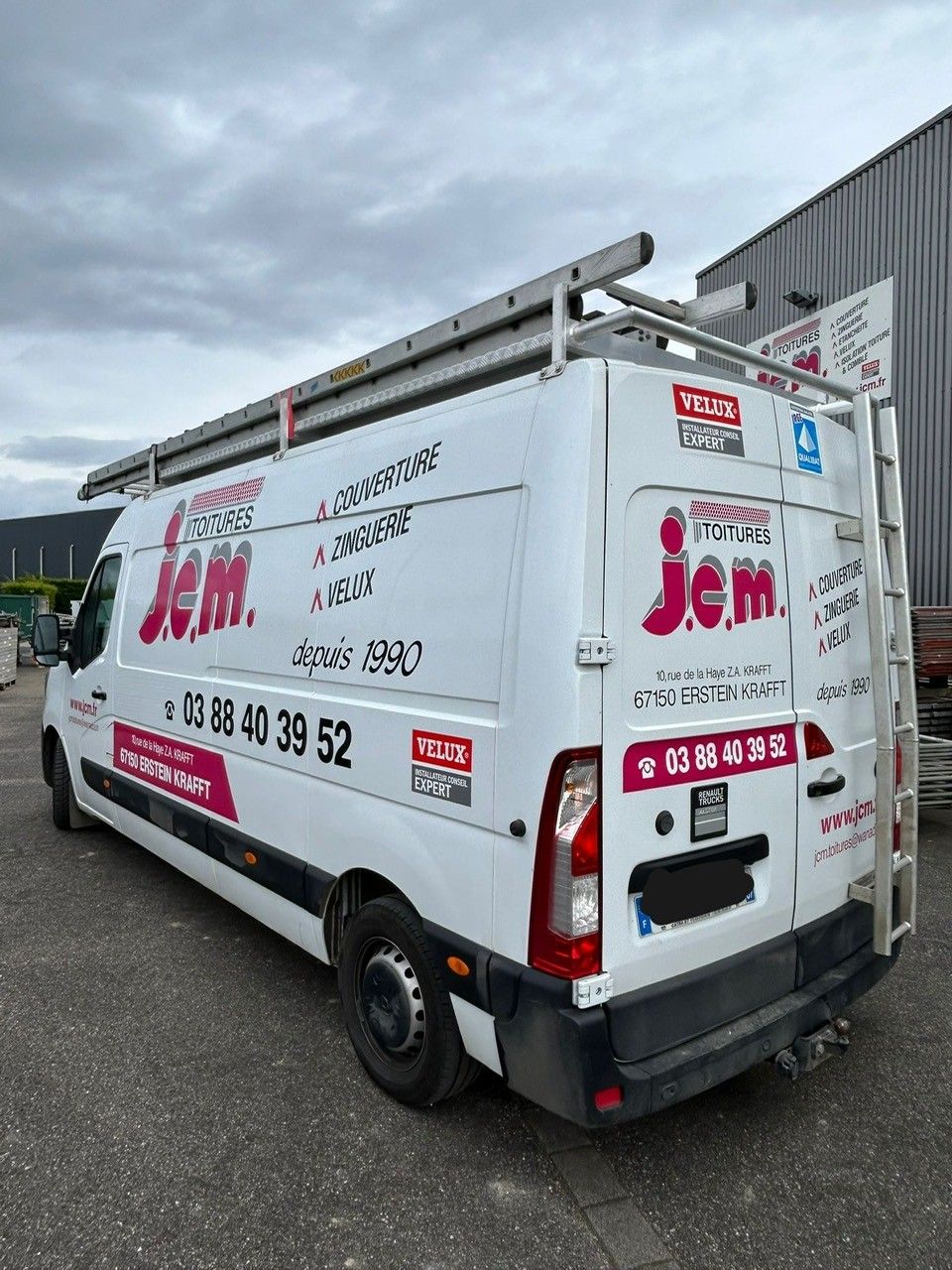 Une camionnette blanche est garée près d'une maison avec un toit en tuiles et un puits de lumière.