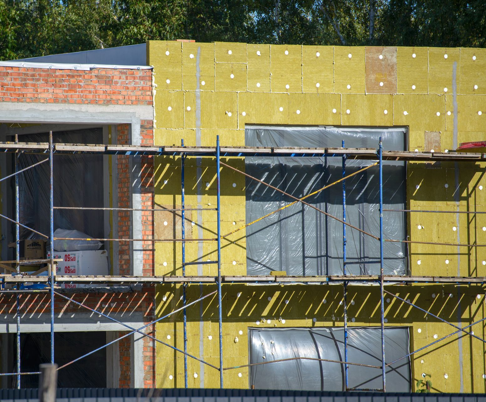 Bâtiment en construction avec isolation, échafaudages et fenêtres protégées.