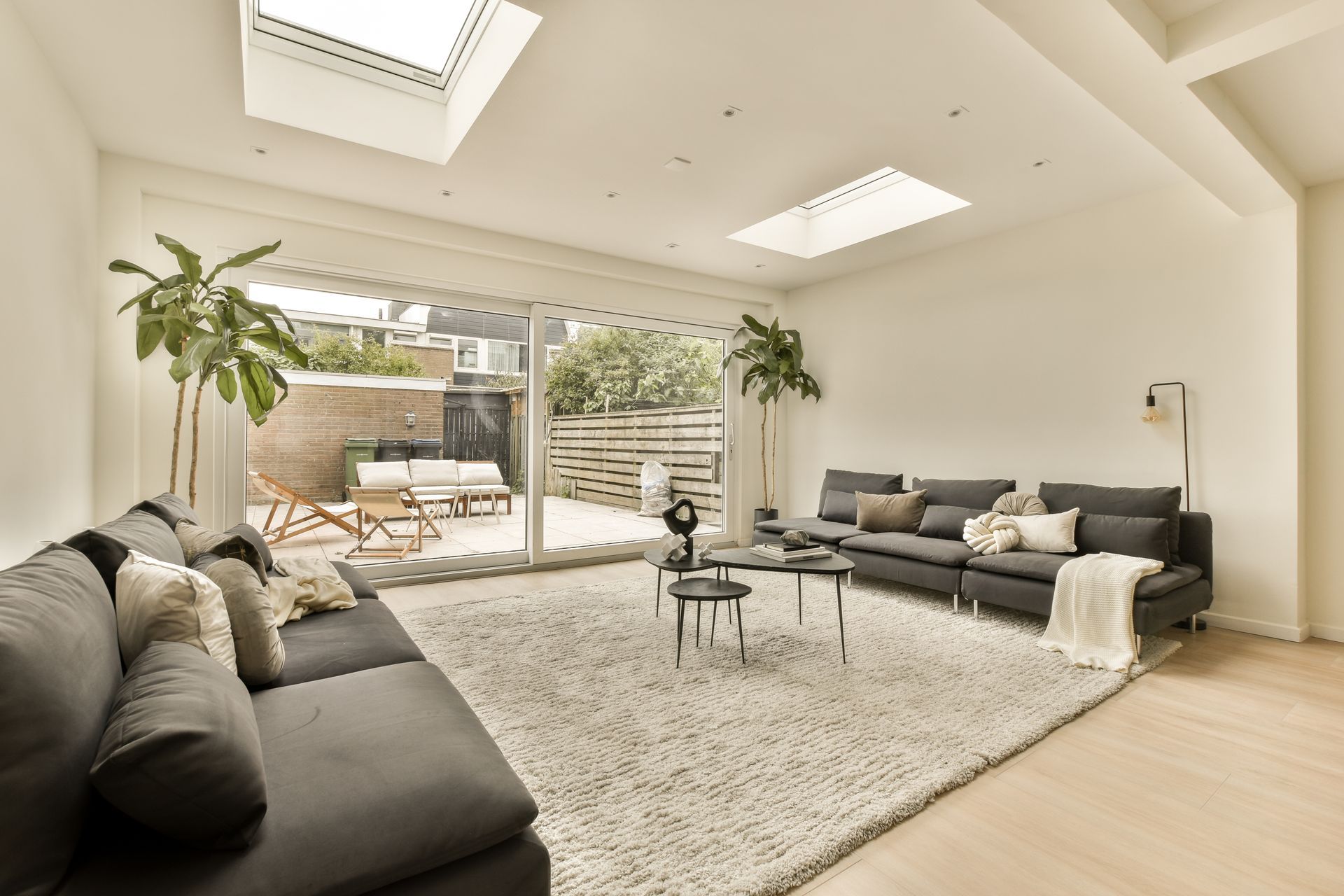 Salon lumineux avec canapés gris, tapis et porte-fenêtre coulissante donnant sur une terrasse.