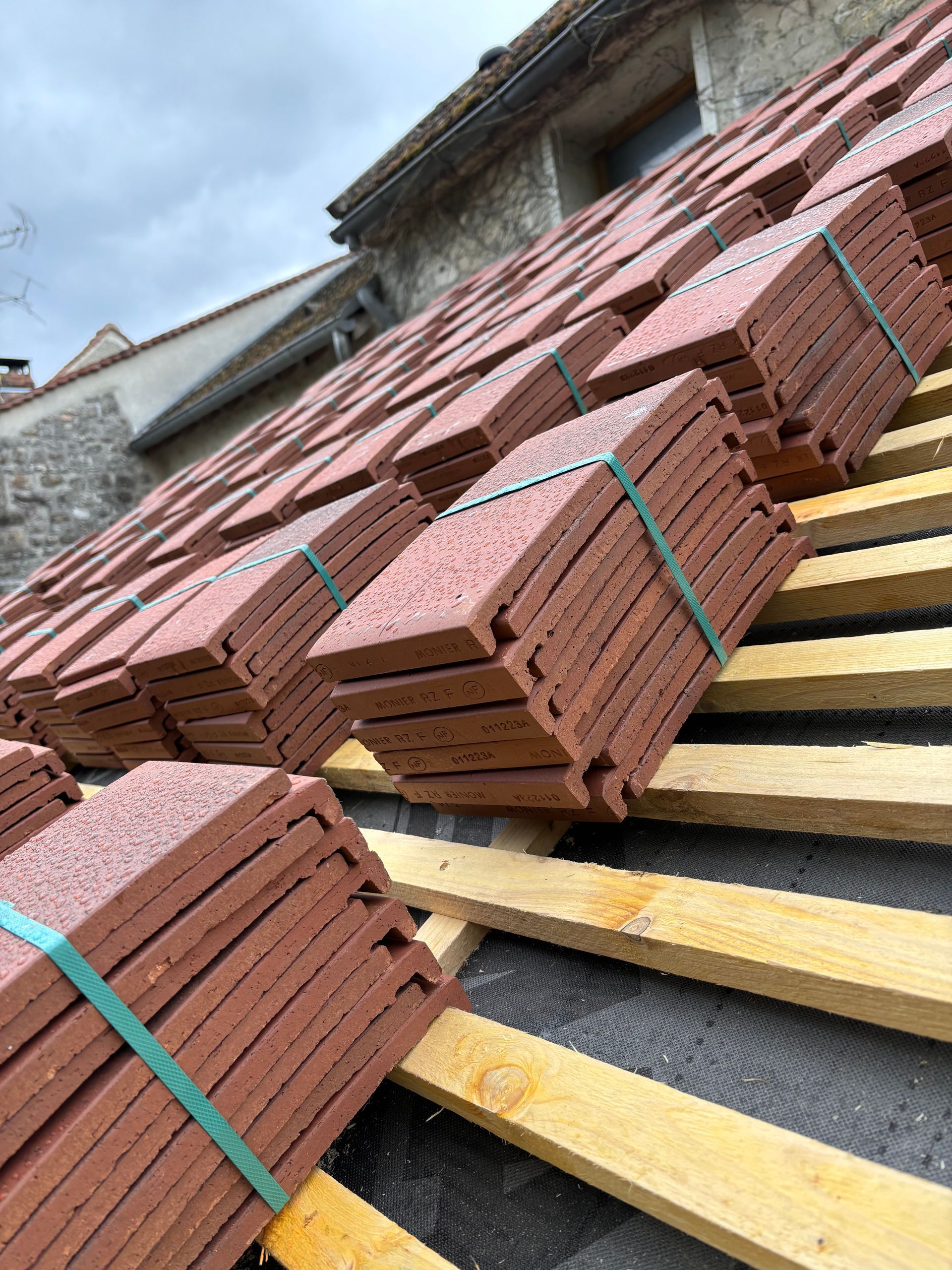 Piles de tuiles rouges sur des poutres en bois, prêtes à être installées sur le toit d'un bâtiment.