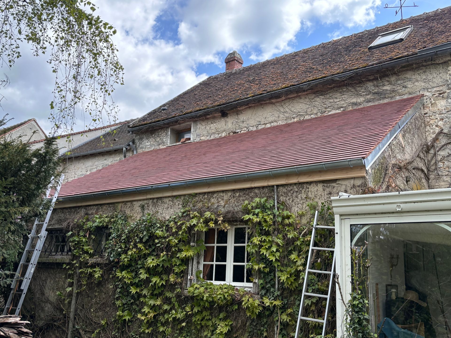 Bâtiment en pierre avec une toiture neuve. Des échelles sont appuyées contre le bâtiment.