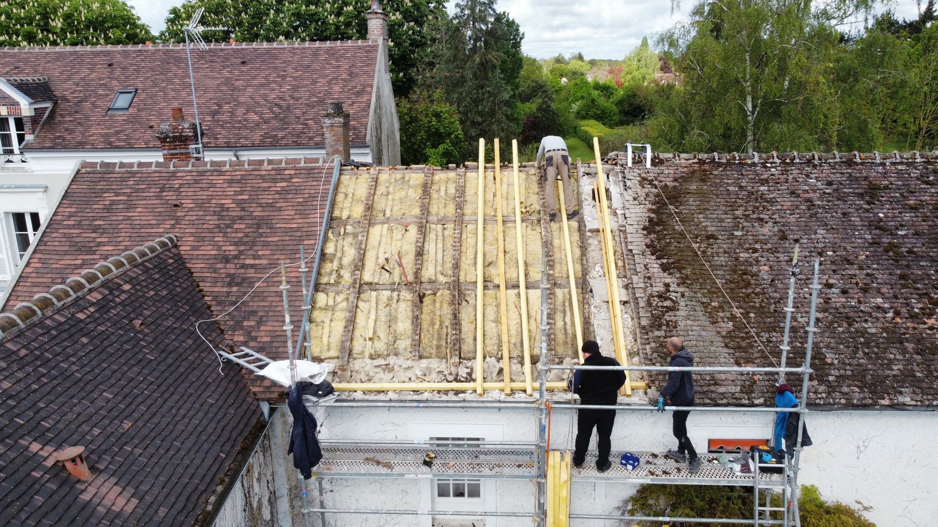 Toiture en construction ; ouvriers sur échafaudages, poutres en bois, toiture partielle.