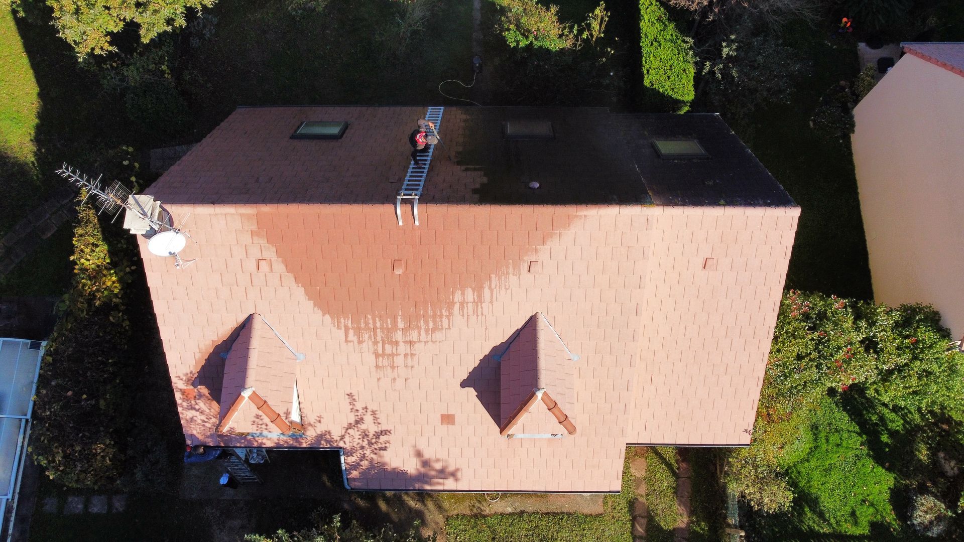 Vue aérienne du toit d'une maison, partiellement mouillé, avec une personne sur une échelle.