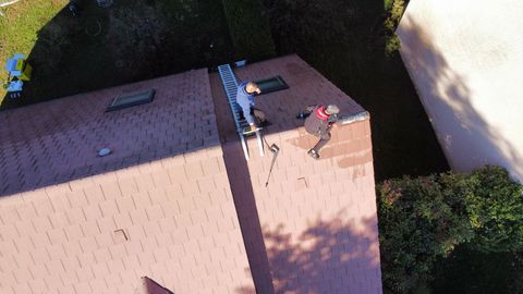 Deux personnes sur un toit rouge ; l'une sur une échelle, l'autre debout près d'une lucarne.