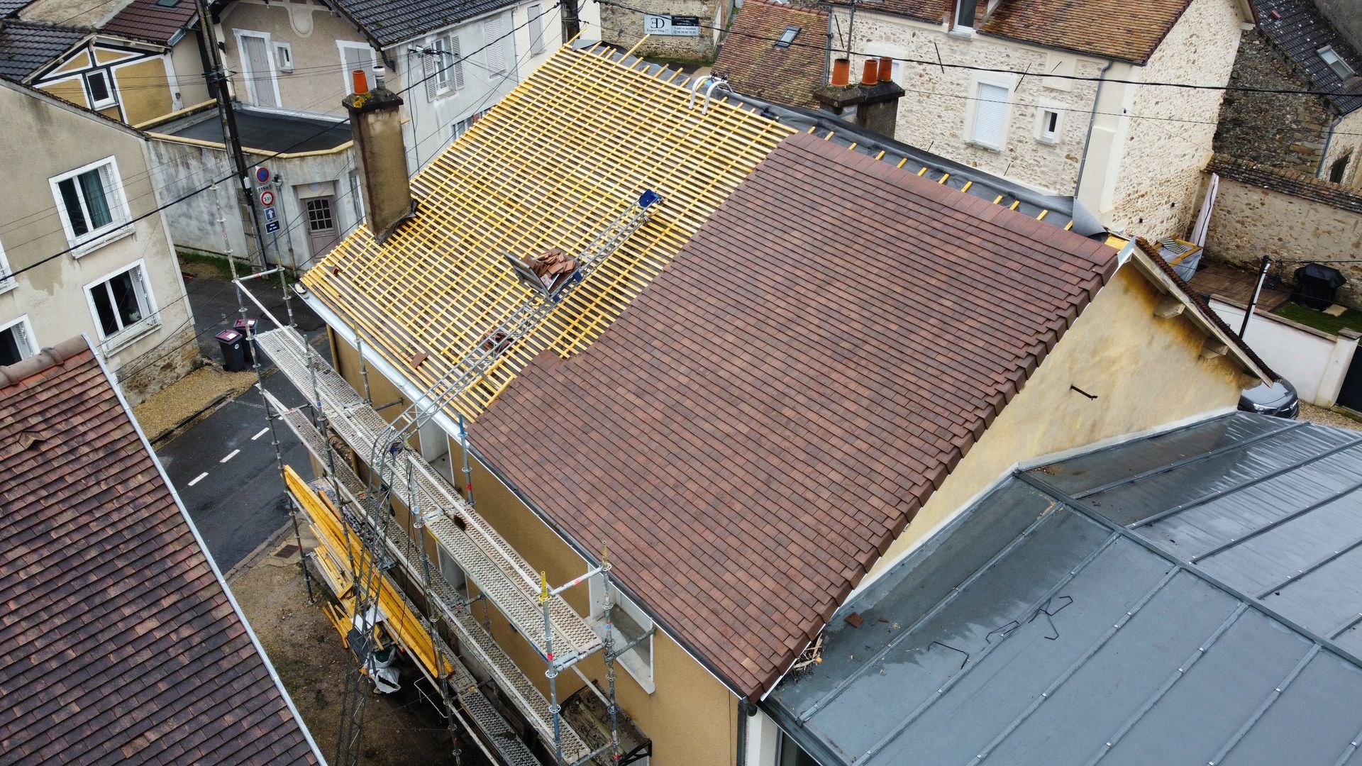 Toiture partiellement recouverte de tuiles rouges ; ouvriers sur un échafaudage à côté de la structure.