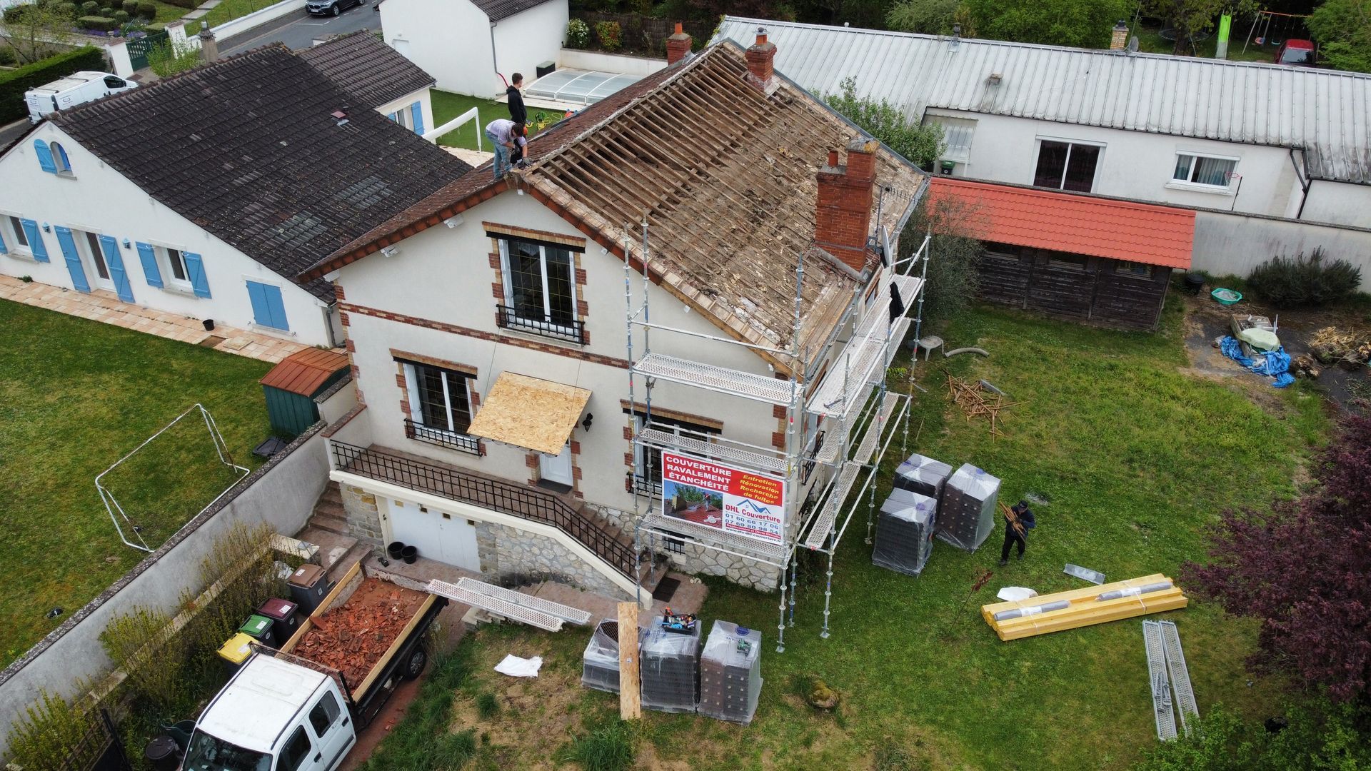 Maison en cours de rénovation de toiture, échafaudages et matériaux visibles dans la cour.