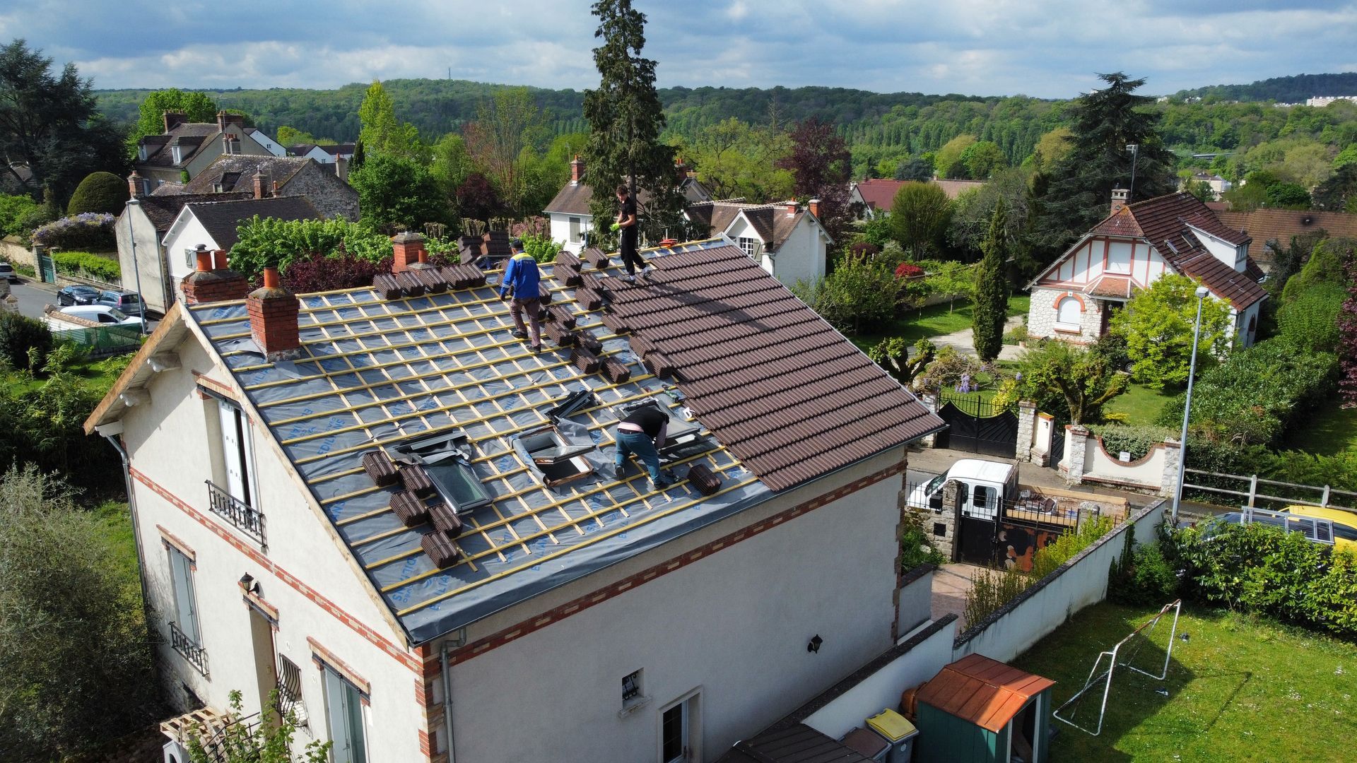 Des couvreurs remplacent les tuiles d'un toit dans un quartier résidentiel.