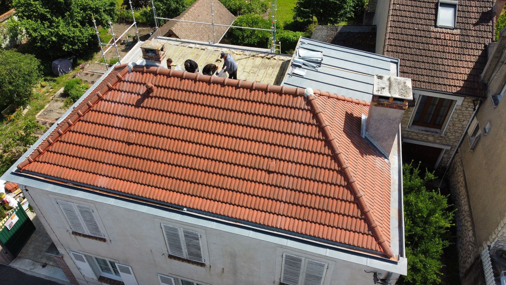 Maison au toit de tuiles rouges avec une cheminée et personne travaillant sur le toit.