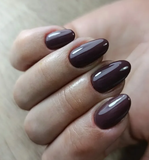 Un primer plano de las uñas de una mujer con esmalte morado oscuro.