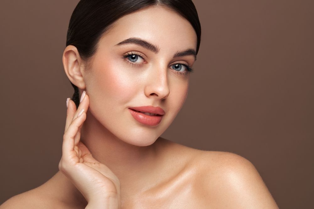 Una mujer se toca la cara con la mano y mira a la cámara.