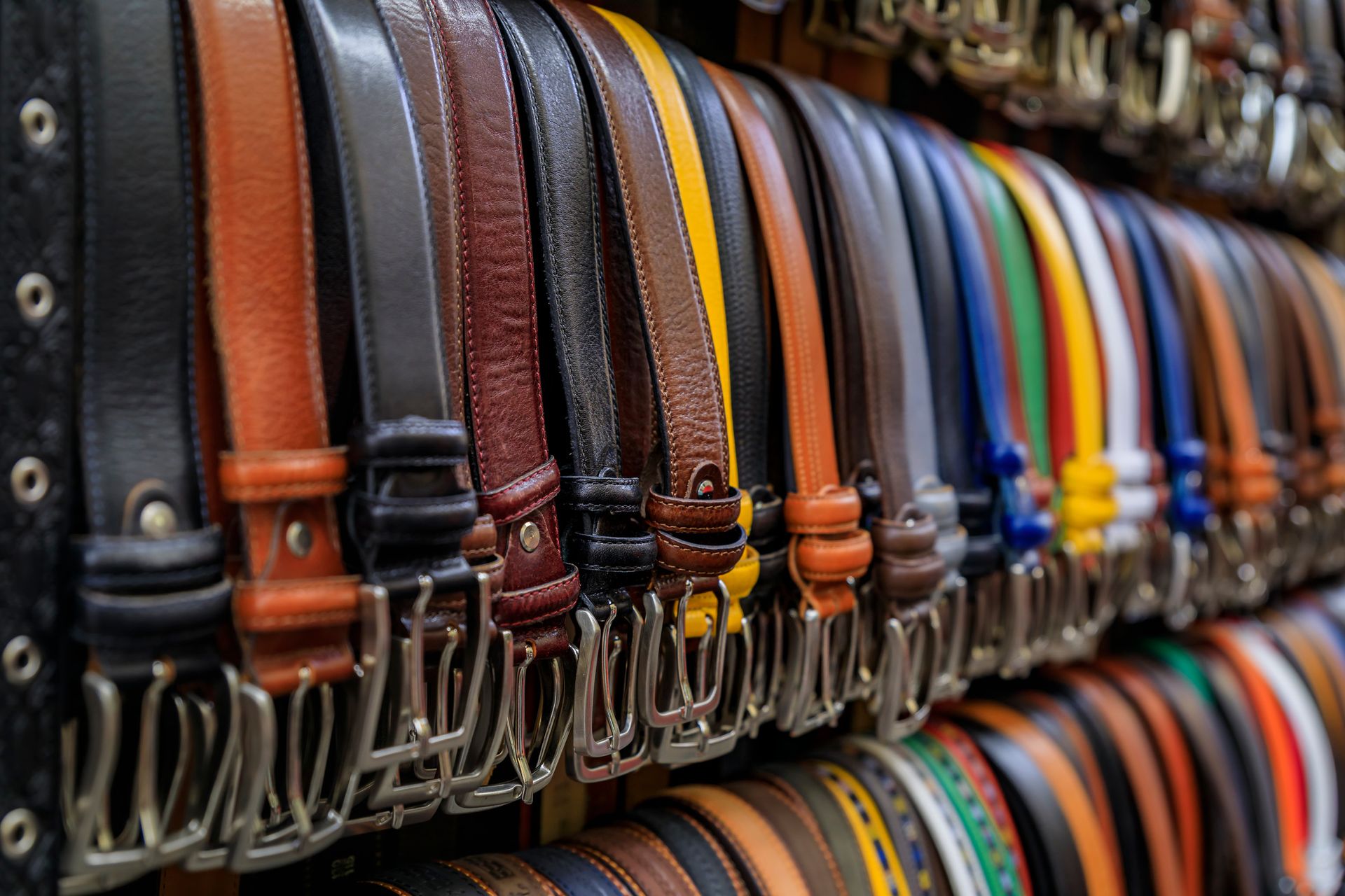 Una fila de cinturones de diferentes colores están alineados en un estante de una tienda.