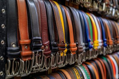 Una fila de cinturones de diferentes colores están alineados en un estante de una tienda.