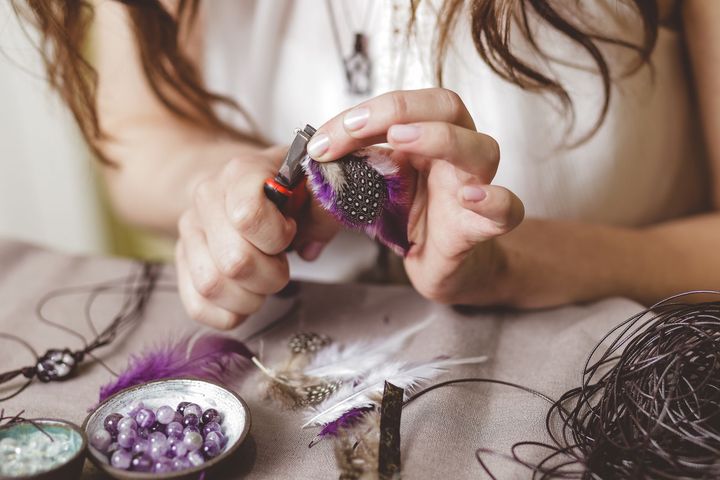 Una mujer está haciendo un collar con cuentas moradas y plumas.