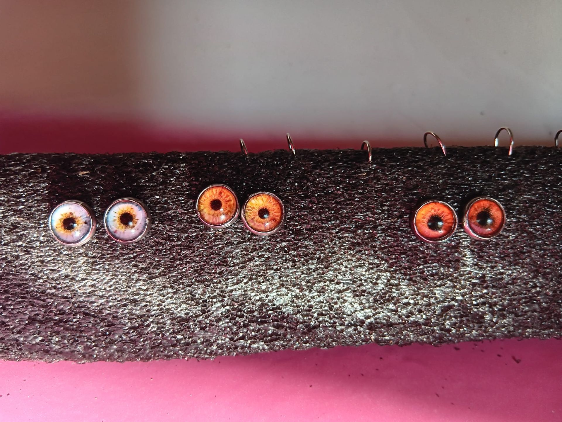 Un montón de pendientes están sobre una superficie rosa.