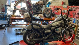 Deux motos sur des supports de travail à l'intérieur d'un atelier bien équipé, avec des murs à outils rouges.