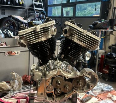 Un moteur de moto bicylindre en V partiellement assemblé, avec des cylindres noirs, repose sur un établi