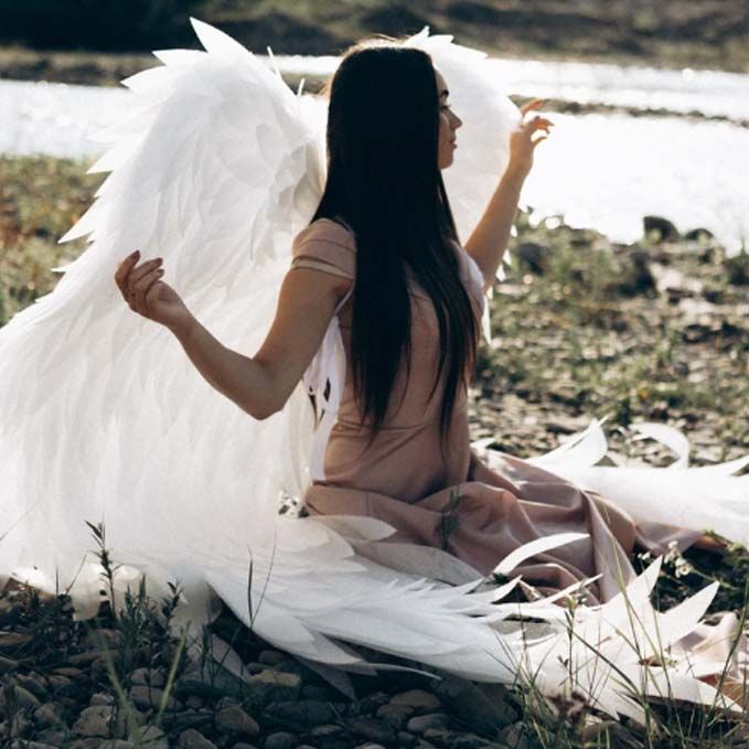 Una mujer con alas de ángel está sentada en el suelo.
