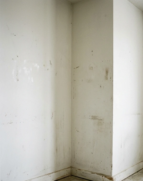 Coin intérieur blanc avec des murs et une plinthe éraflés, présentant des taches et des traces d’usure.