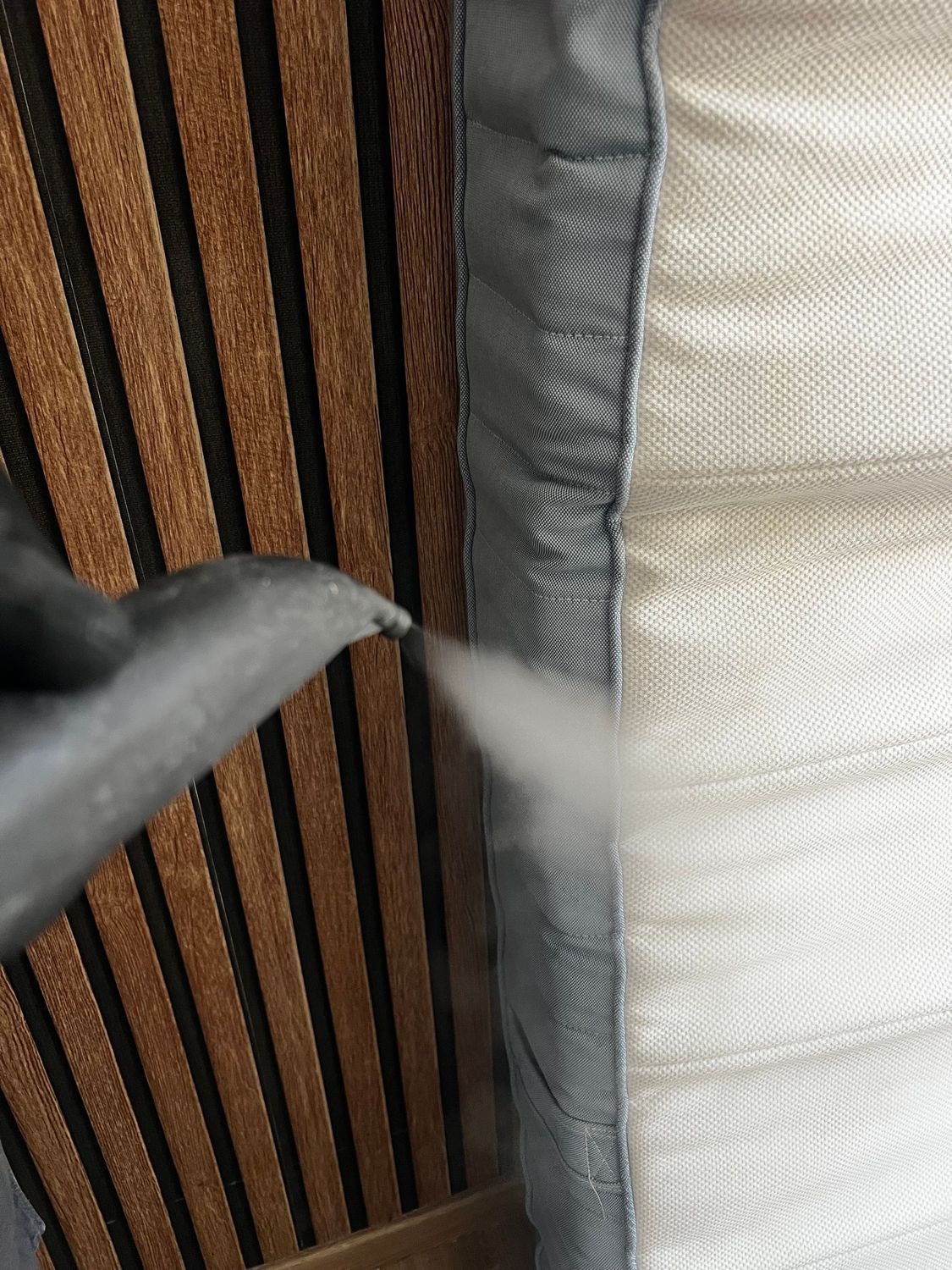 Gros plan d'un panneau de lattes de bois à côté d'un tissu gris et d'une surface blanche, avec un objet flou au premier plan