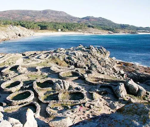 Un acantilado rocoso con vista a un cuerpo de agua con montañas al fondo.