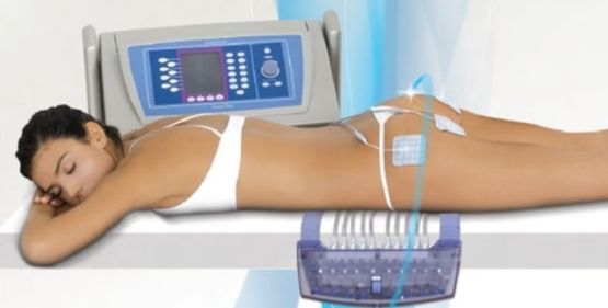 Una persona yace boca abajo sobre una camilla recibiendo un tratamiento estético de estimulación muscular eléctrica mediante electrodos aplicados en los glúteos.