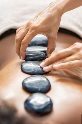 Las manos de una persona colocan piedras de masaje lisas y oscuras en fila a lo largo de la espalda de otra persona.