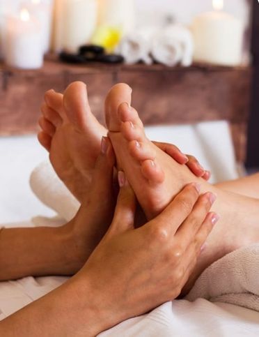 Una persona recibe un relajante masaje de pies en un ambiente de spa, con velas y toallas de fondo.