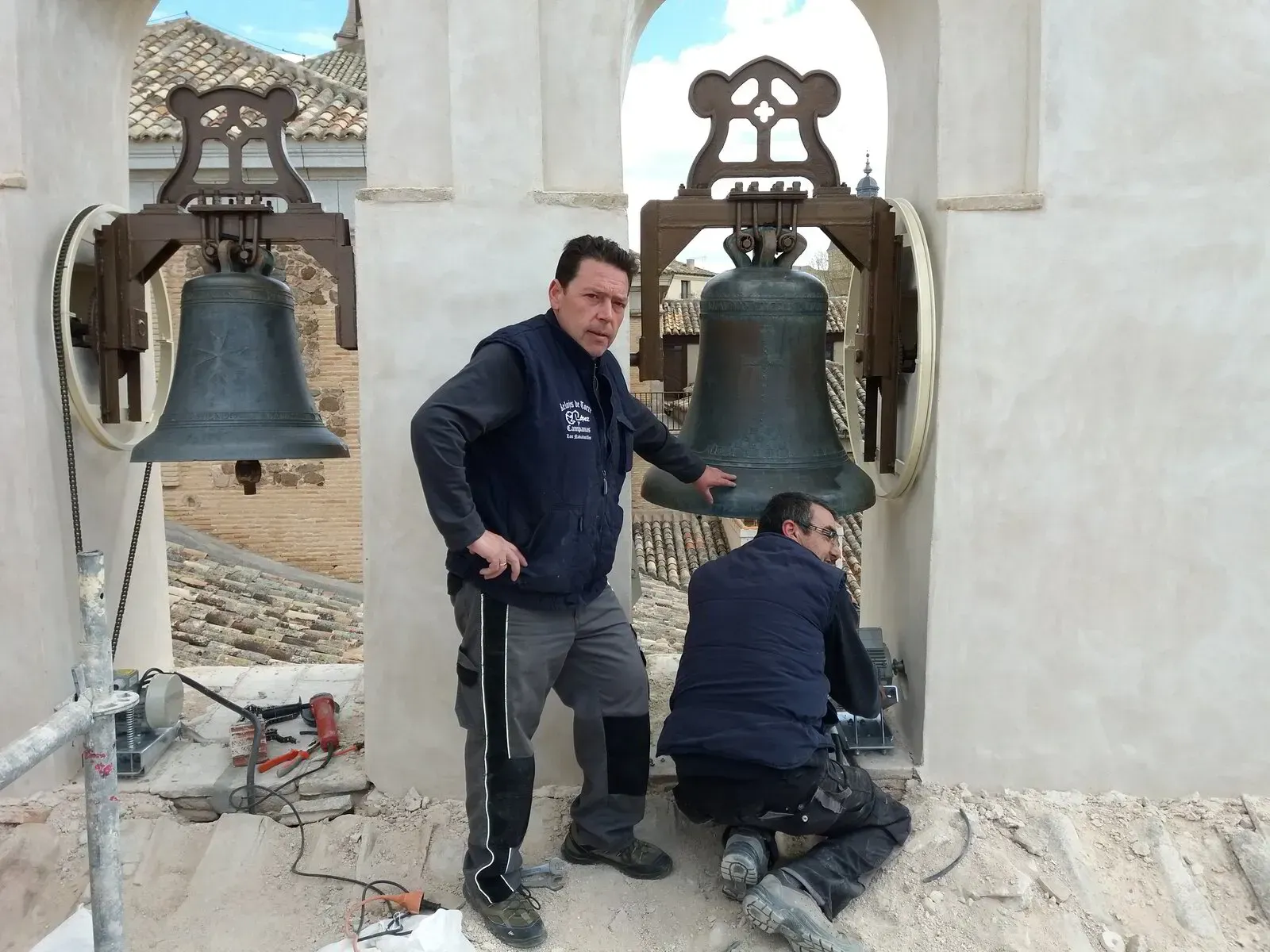 Dos hombres están trabajando en un campanario y uno tiene la letra e en su chaleco.