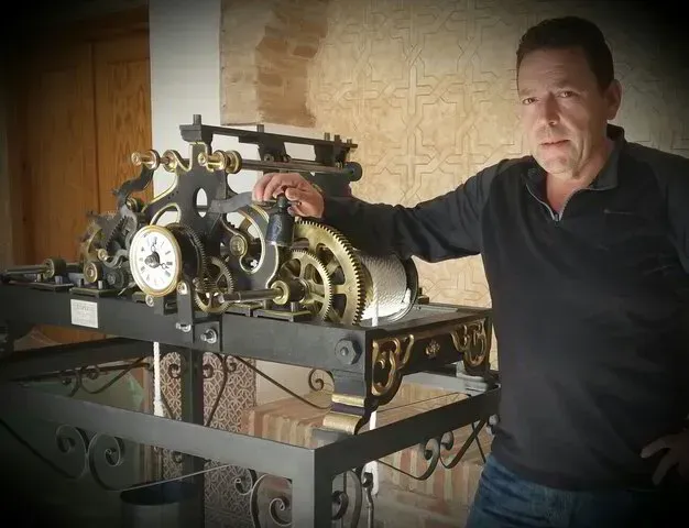 Un hombre con un suéter negro está de pie junto a un reloj.