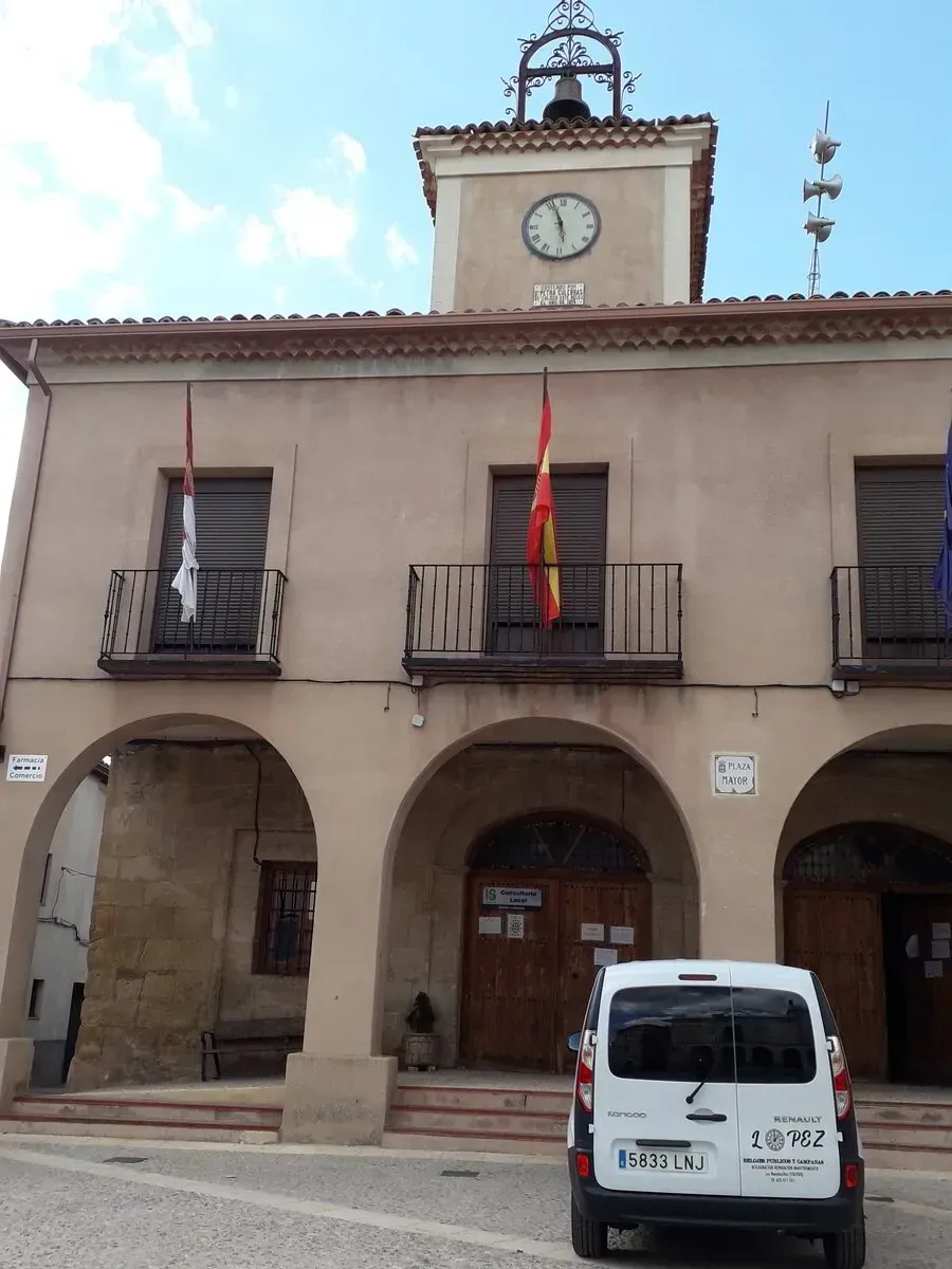 Una camioneta blanca está estacionada frente a un edificio con un reloj en la parte superior.