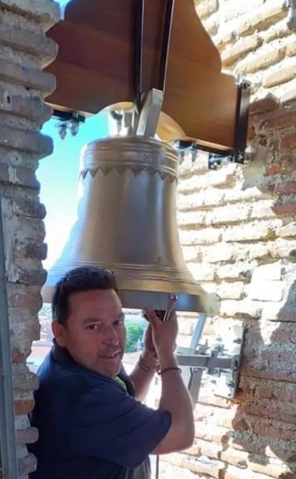 Un hombre sostiene una campana grande frente a una pared de ladrillos.