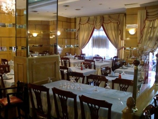Interior de restaurante con mesas preparadas para cenar; paneles de madera y cortinas decorativas.